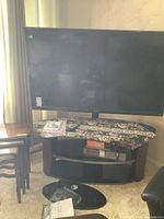 Full view of Sharp AQUOS TV on curved two-tier stand, manuals and remote on top, oval base foot in front.