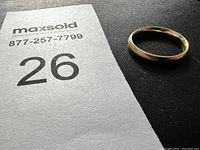Gold band ring placed on black textured surface alongside a number card that reads 26.