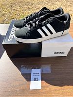 Pair of black Adidas shoes with white stripes and sole shown on original Adidas shoe box, size 12.