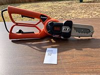 Full side view of the Black and Decker Alligator chainsaw showing orange and black colors, handles, electric cord and the blade guard.