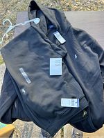 Full view of black hooded jacket and jogger pants laid flat, showing Ralph Lauren Polo player logo embroidered in white on both pieces, tags still attached.