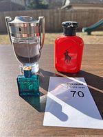 Three cologne bottles including trophy-shaped clear bottle, red Polo Ralph Lauren, and dark teal Versace with MaxSold tag