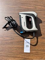 Full view of electric handheld stapler with attached black power cord on a wooden surface under sunlight.