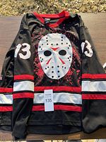 Front view of black Friday The 13th hockey jersey with large white hockey mask graphic and number 13 on sleeves