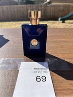 Front view of deep blue rectangular cologne bottle with gold emblem on a wooden surface outdoors.