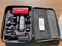 Massage gun and attachments neatly arranged in open black case with custom foam cutouts.