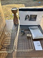 Photo showing wire baskets, wooden item, packaged sheets and pillowcases on table outside.