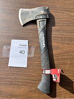 Husky camp axe hatchet with black handle lying flat on wood surface showing the full hatchet and seller label 40 beside it.