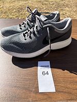 Pair of gray Nike tennis shoes with black swoosh, size 12, displayed on wooden surface in daylight.