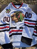 Full front view of white Chicago Blackhawks hockey jersey with team logos and numbers, size XL tag visible.