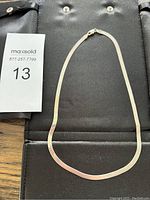 Full view of sterling silver flat necklace laid on black background.