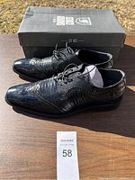 Pair of black Stacy Adams men's dress shoes displayed on wooden table with original shoebox in background.