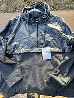 Black Under Armour pullover hoodie laid flat on a wooden surface outdoors, with a lot card indicating lot 150.