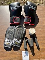 Full set of Everlast boxing gear on wooden table, including gloves, palm protectors, hand wraps, and grip strengtheners