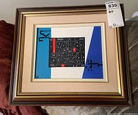 Framed artwork full view propped on sofa showing overall composition and frame.