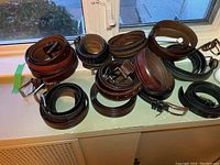 Overview photo showing 11 belts in brown, black leather and fabric, rolled and laid out on windowsill.