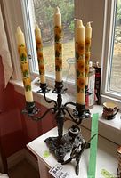 Photo of large five-arm metal candle holder with sunflower candles, showing the intricate base with pond motif.