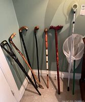 Group shot of six wood canes, one metal walking cane, and one butterfly net.