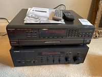 Stacked view of Technics CD player on Yamaha receiver with two remotes and manuals on top