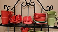 Complete view of assorted Fiesta Ware red and green teacups, saucers, dessert plates, bowls, and mugs arranged on a black metal rack.