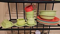 Full set of Fiesta Ware dinnerware including stacked plates, soup cups, bowls, cream and sugar set, and butter dish shown on metal rack.