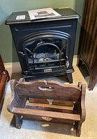 Black Decorflame electric stove heater and rustic wood magazine rack side by side on carpeted floor.