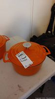 Photo showing the orange enamelled cast iron Dutch oven with lid and tag labeled '946 Le Cuistot Dutch oven'.