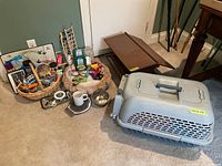 Photo showing entire pet supplies lot including Dog It plastic pet carrier, wooden bird feeder, pet bed with cushion, various grooming tools, cat toys, water dish, and baskets of accessories