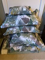Stack of pillows and folded queen duvet cover with tropical leaf pattern, showing fabric colors and design.
