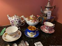 Overview of lot showing multiple porcelain teacups, saucers, teapots, and silver-plated teapot