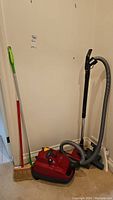 Wide view showing red SEBO canister vacuum next to push broom