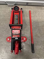 Top view of red hydraulic trolley jack with detachable handle shown separately.