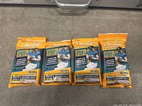 Four sealed orange packs of Panini Prestige 2022 NFL trading cards laid on a flat surface showing the front of each pack with player image and text.