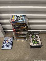 Stack of PlayStation 3 game cases with Tom and Jerry DVD sleeve and separate PC game case Battlefield 2.