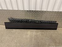 Full view of Sony soundbar, black, positioned on diamond plate metal background.