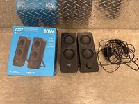 Photo showing two black Logitech speakers and the original blue product box on a wooden surface.