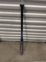 Full view of a Stealth brand baseball bat standing vertically against a storage unit door showing the bat's details and branding.