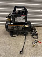 Full view of the Team Mechanix air compressor with attached coiled air hose and metal blow gun resting on concrete floor.