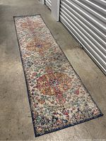 Full view of worn vintage carpet runner laid flat on concrete floor, showing entire length and pattern.