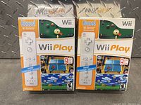 Two sealed Nintendo Wii Play game packages each including a Wii Remote controller.