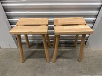 Front view of four wooden stools showing the rectangular top surfaces and three angled legs.