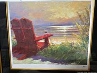 Full view of the framed beach painting showing red chairs, grassy foreground, and ocean sunset.