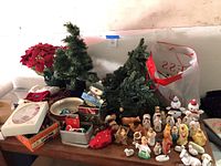 Wide view of Christmas decorations including two small artificial trees, ceramic nativity figurines, stockings, baubles, and poinsettia plant.