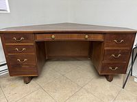 Front view of the wooden corner desk showing six drawers with brass handles and wood finish with minor scratches.
