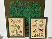 Two smaller framed crewel embroidery art panels with floral, owl, bird, and butterfly motifs in front of a large tree embroidery.