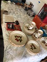 Wide view of table showing Mikasa Strawberry dishes, assorted glassware, silverplate pieces, candlesticks, and tools