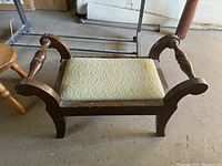 Wooden footstool with cream floral padded seat, curved wooden arm supports, showing style and wear