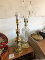 Two brass table lamps without shades and one glass floor lamp without shade on a wooden surface.