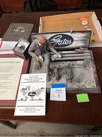 Full view of the Michael Garman sculpture showing man feeding dogs on bench with 'Gates' sign, alongside documentation and pins tray.