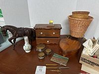 Photo showing a dark brown horse figurine, a rectangular wooden box with two drawers, heart-shaped box, wicker basket, small decorative vase, three small glass jars with brass lids, sewing scissors, thread snipper, and a horse racing collectible card.